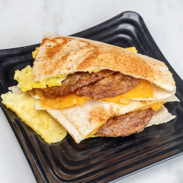 A breakfast quesadilla with scrambled eggs, sausage patties, and melted cheese on a black plate.