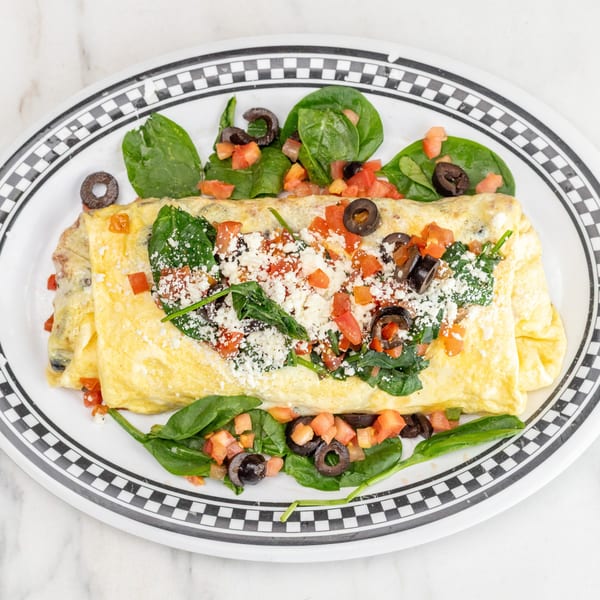 A diner omelet filled with spinach, tomatoes, olives, and feta cheese, served on a checkered plate.