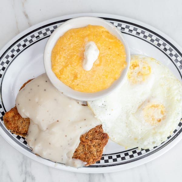 University Diner's chicken fried steak with gravy, two fried eggs, and a side of grits.