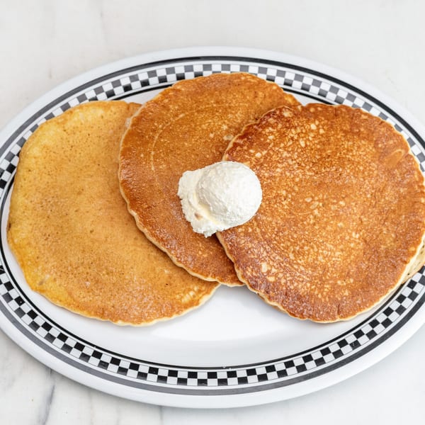 Three golden pancakes with a dollop of whipped cream on a diner-style checkered plate.